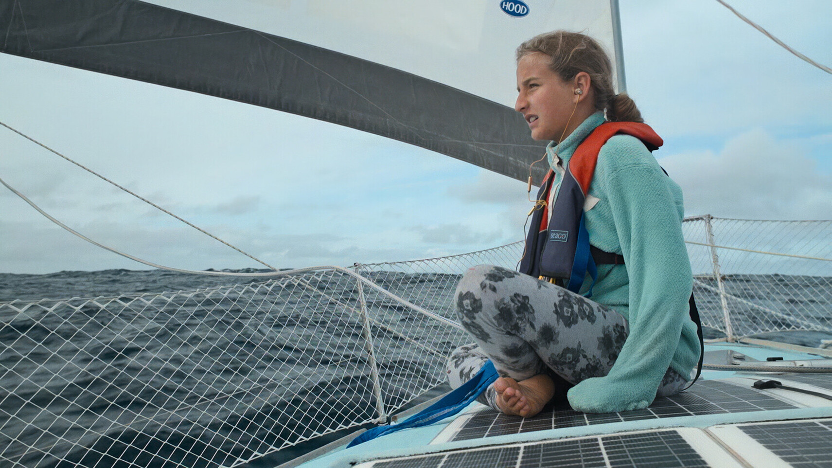 Salina Schw&ouml;rer sitzt auf dem Deck des TOPtoTOP Expeditions-Katamarans mit Schwimmweste, barfu&szlig;, und blickt w&auml;hrend einer Offshore-Passage auf den Meereshorizont